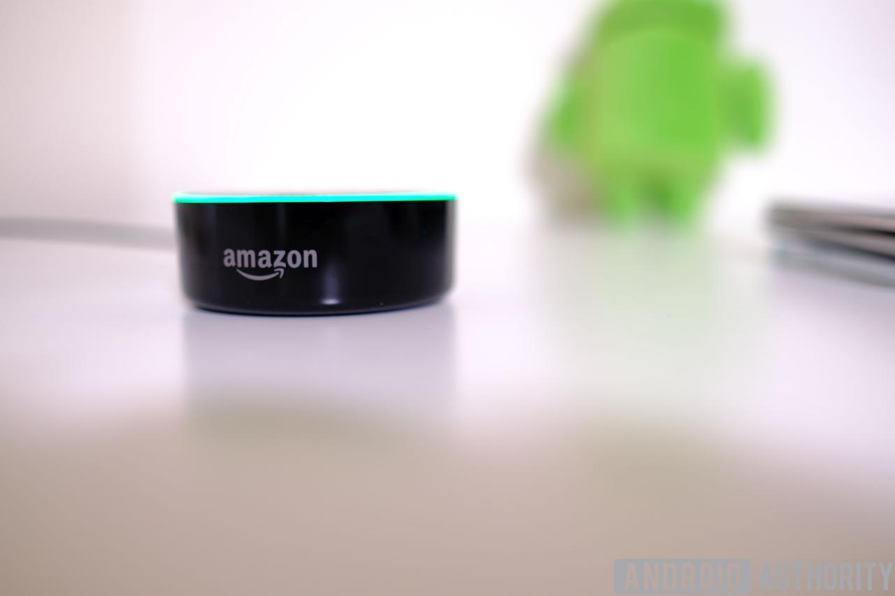 Imagen de Amazon Echo Dot en una superficie blanca con una figura de Android en el fondo.