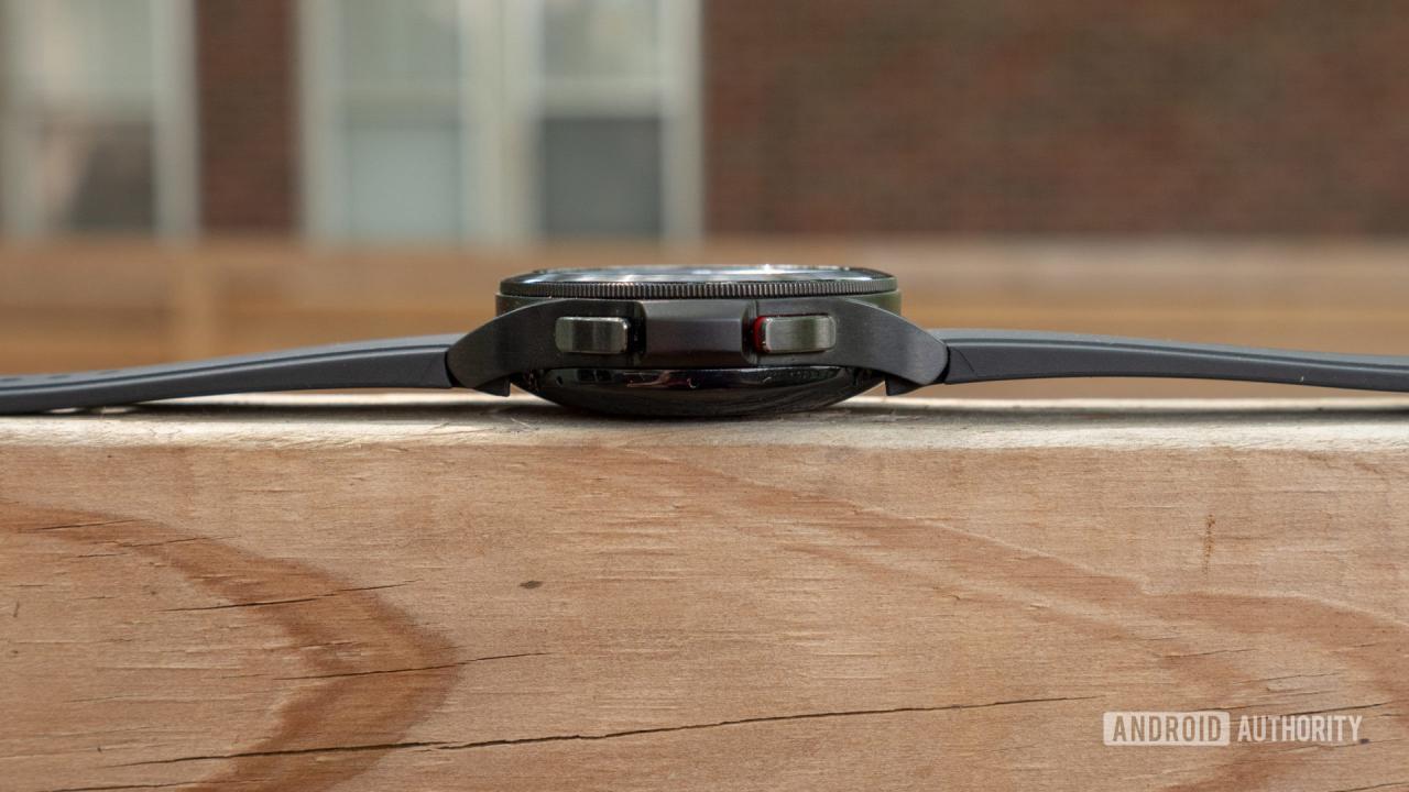 El Samsung Galaxy Watch 4 Classic acostado sobre una valla mostrando sus botones laterales y su bisel giratorio.